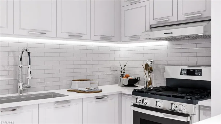 Kitchen with stainless steel gas stove, decorative backsplash, under cabinet range hood, white cabinets, and light stone countertops
