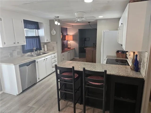 Kitchen featuring white appliances, a sink, a peninsula, white cabinets, and recessed lighting