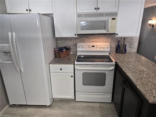 Kitchen with white appliances, white cabinets, and tasteful backsplash