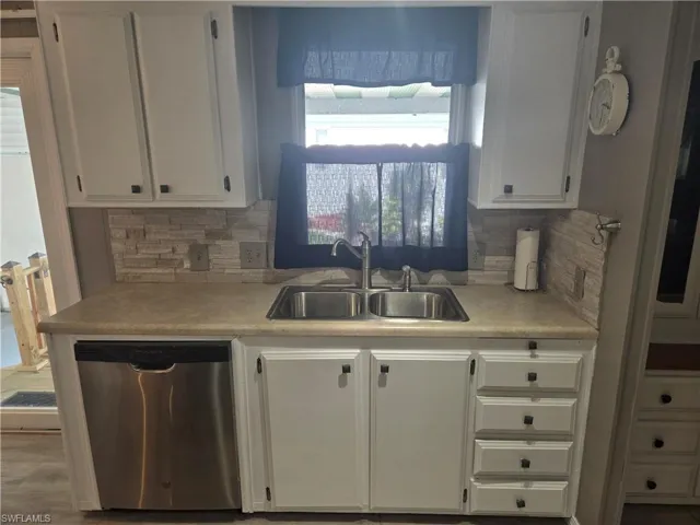 Kitchen with stainless steel dishwasher, a sink, white cabinets, and light countertops