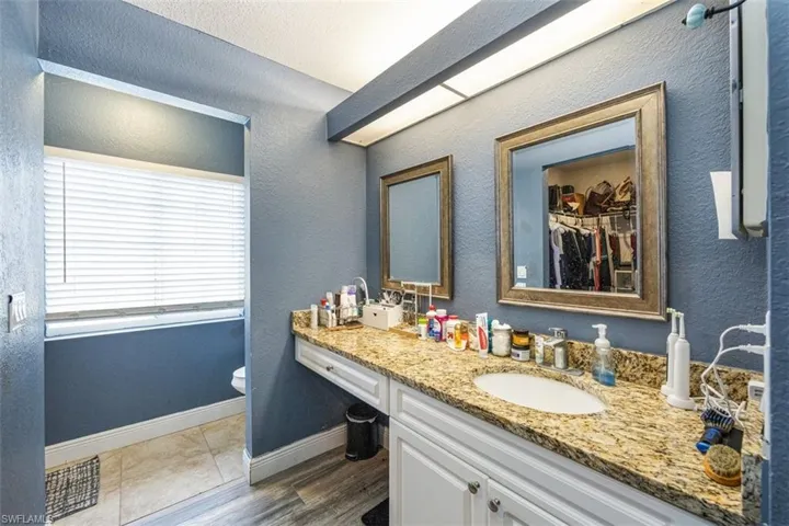 Bathroom with a textured wall, vanity, a spacious closet, dark tile patterned floors, and a textured ceiling