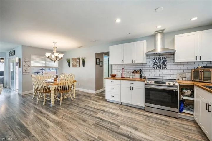 Kitchen featuring butcher block counters, electric range, white cabinetry, tasteful backsplash, and wall chimney exhaust hood