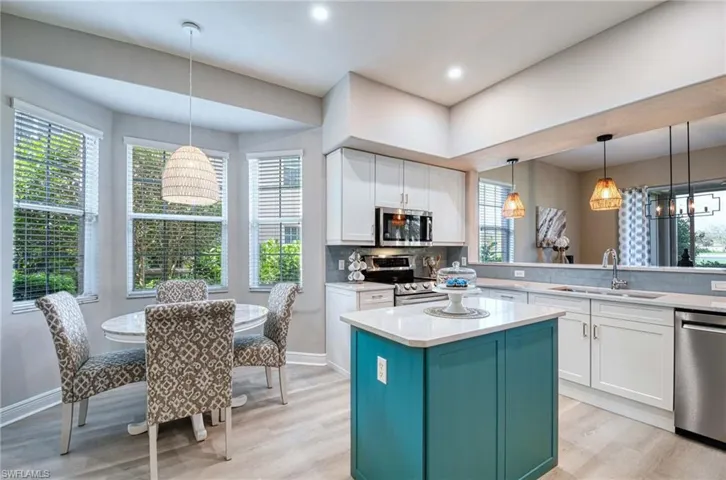 Kitchen featuring stainless steel appliances, white cabinetry, sink, hanging light fixtures, and a kitchen island