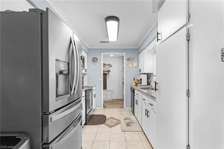 Kitchen with stainless steel refrigerator, light tile patterned floors, and white cabinetry