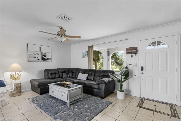 Living area with light tile patterned floors, ceiling fan, and ornamental molding