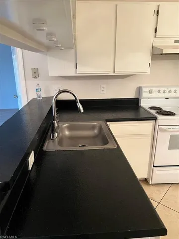 Kitchen with black stove, dark countertops, extractor fan, light tile patterned floors, and white cabinetry