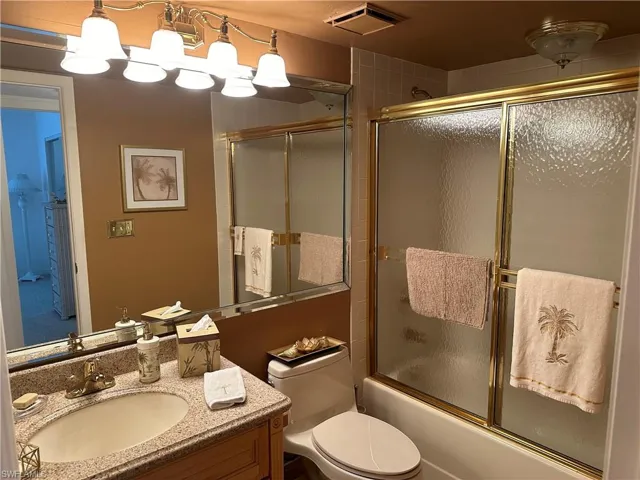 Full bathroom with vanity, bath / shower combo with glass door, and toilet