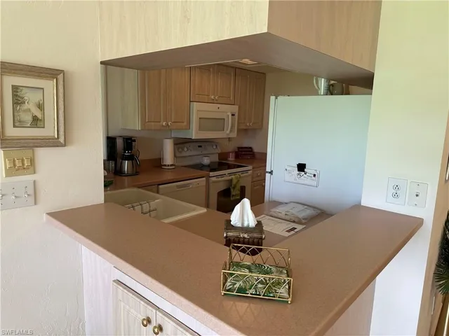 Kitchen featuring light brown cabinetry, sink, kitchen peninsula, and white appliances