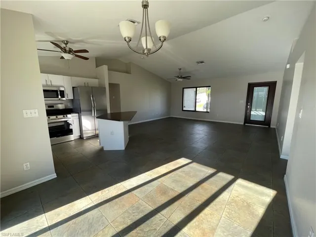 Kitchen with vaulted ceiling, stainless steel appliances, open floor plan, white cabinetry, and pendant lighting