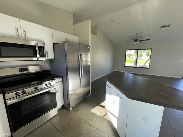 Kitchen with stainless steel appliances, white cabinetry, lofted ceiling, butcher block countertops, and open floor plan