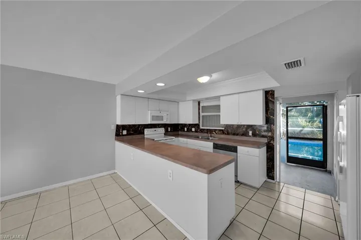 Kitchen with white cabinetry, a peninsula, white appliances, tasteful backsplash, and light tile patterned floors