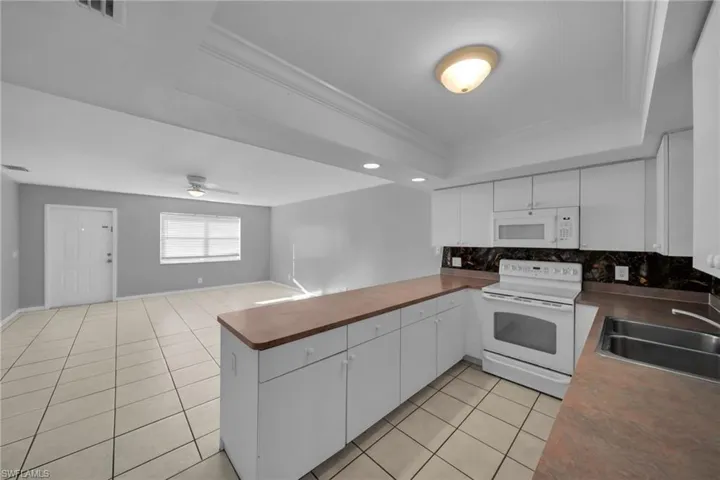 Kitchen with white appliances, a peninsula, white cabinets, dark countertops, and open floor plan