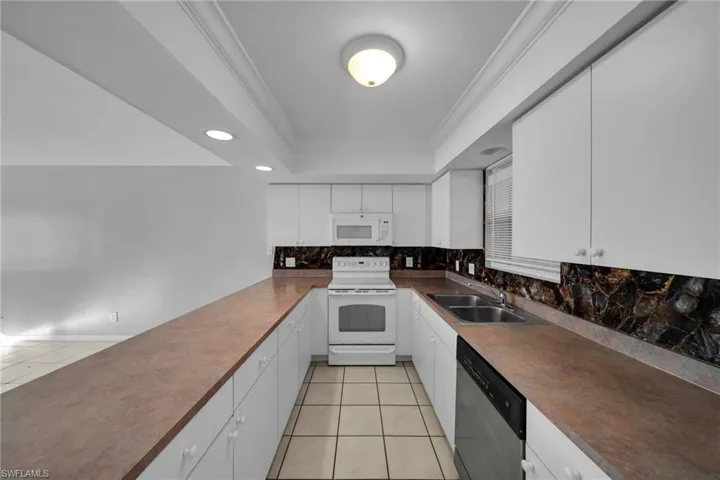 Kitchen featuring white appliances, backsplash, dark countertops, ornamental molding, and a peninsula
