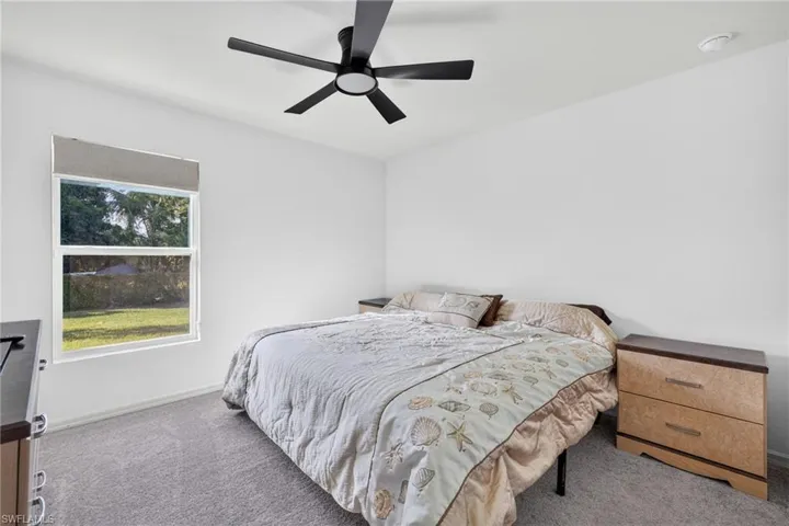 Neutral interior featuring carpeting, a matte black multi-blade ceiling fan with integrated lighting, and a single-hung window with a neutral-toned valance