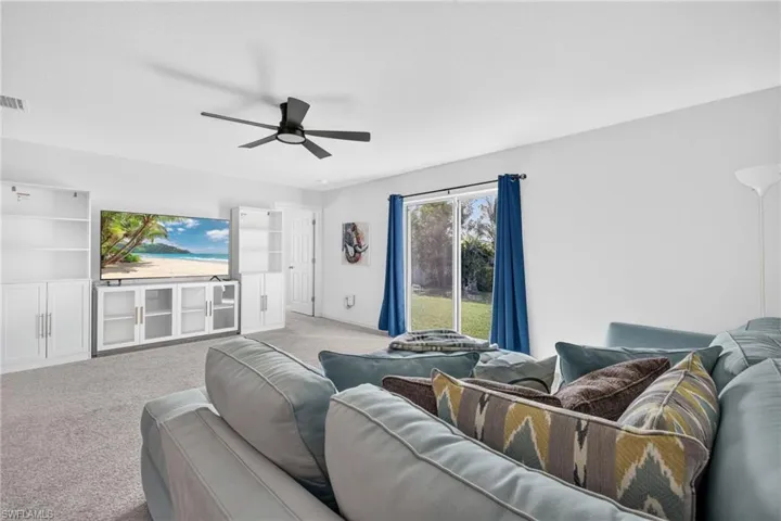 Living space featuring white built-in cabinetry, neutral wall-to-wall carpeting, a multi-blade ceiling fan, and a sliding glass door providing natural light
