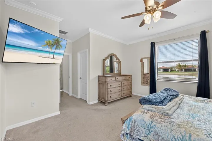 Bedroom with light colored carpet, ornamental molding, and a ceiling fan
