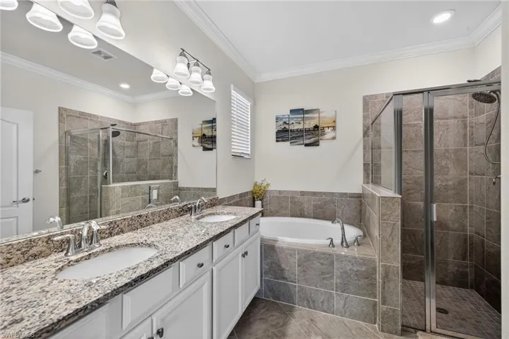 Full bath featuring crown molding, double vanity, a garden tub, a stall shower, and recessed lighting