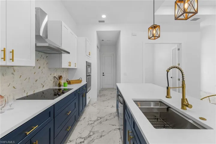 Kitchen with white cabinets, blue cabinetry, decorative backsplash, wall chimney exhaust hood, and recessed lighting