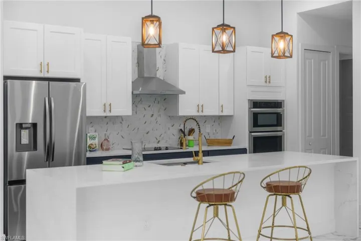 Kitchen featuring stainless steel appliances, backsplash, a center island with sink, light countertops, and a breakfast bar area