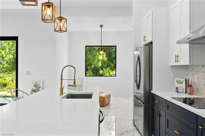 Kitchen with white cabinetry, light countertops, light marble finish floors, freestanding refrigerator, and backsplash