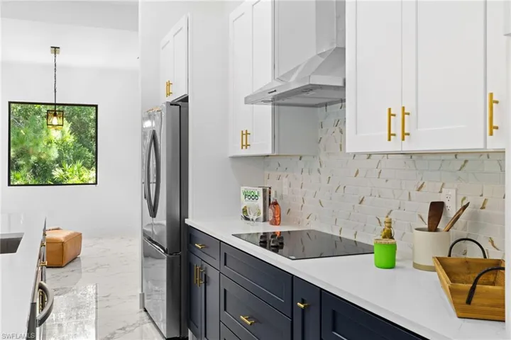 Kitchen featuring white cabinetry, wall chimney exhaust hood, light countertops, and freestanding refrigerator