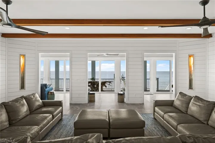 Tiled living area with ceiling fan, beamed ceiling, a water view, wooden walls, and recessed lighting