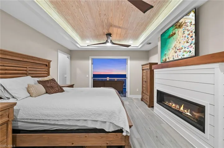 Primary bedroom featuring recessed wood ceiling, french doors to third floor balcony,  light grey finished floors, 2  ceiling fans, remote control propane fire place.