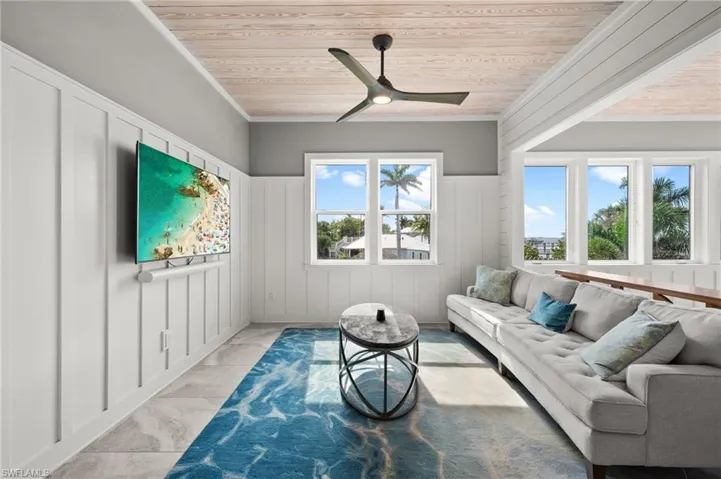 Living area featuring light marble finish flooring, wood ceiling, a decorative wall, a ceiling fan, and wainscoting