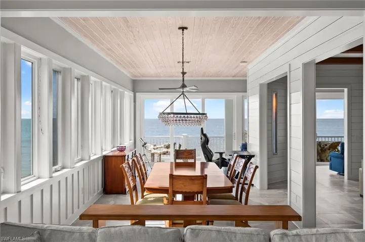 Dining space with a chandelier, a water view, wood recessed ceiling, shiplap walls and Hellfire 360 contemporary gas fireplace mounted in the wall.