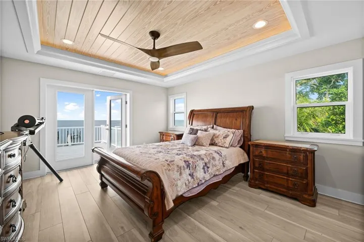 Bedroom with a recessed wooden ceiling, woodgrain ceiling fan, access to exterior second floor balcony by french doors.