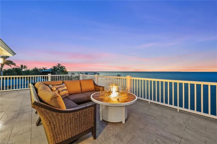 Third floor balcony at dusk with an outdoor living space and fire pit, and a water view.