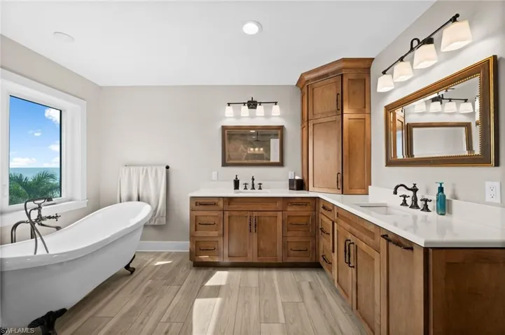 Full bath with double vanity, a freestanding tub, wood finished floors, and recessed lighting