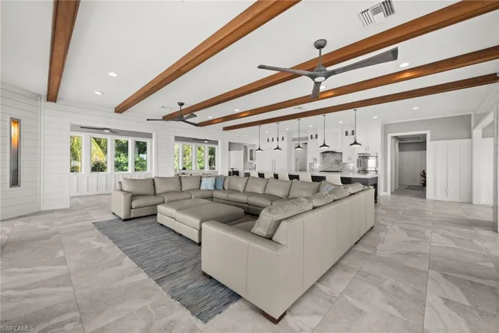 Living room with ceiling fan, beamed ceiling, light marble finish tile floors, shiplap walls and recessed lighting