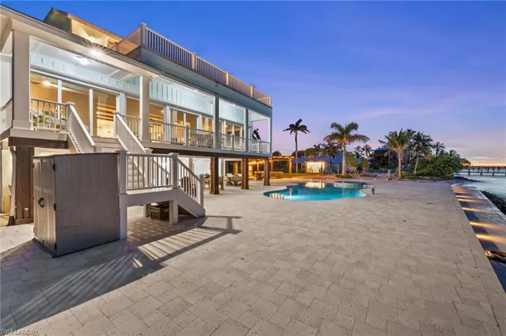 Rear view of house, outdoor pool area with stairs leading to second floor deck and lit pavers.