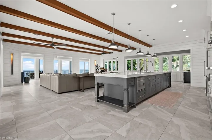 Kitchen with gray cabinetry, light countertops, open floor plan, plenty of natural light, and beamed ceiling