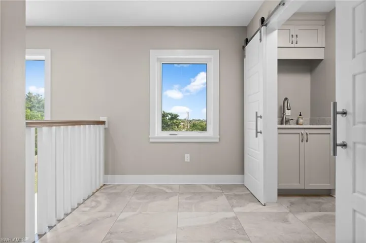third floor hall with picture window, laundry room with sliding white barn doors and a laundry sink with cabinets for storage.