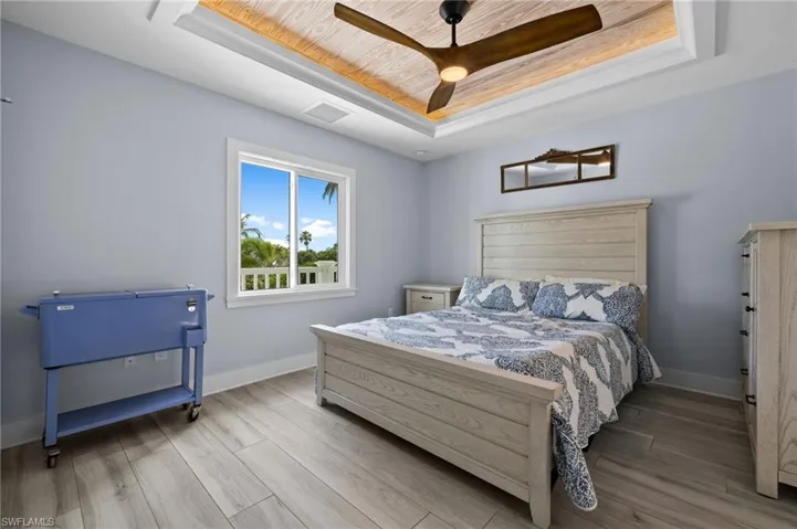 Bedroom with a recessed wood ceiling, grey floors, and woodgrain ceiling fan