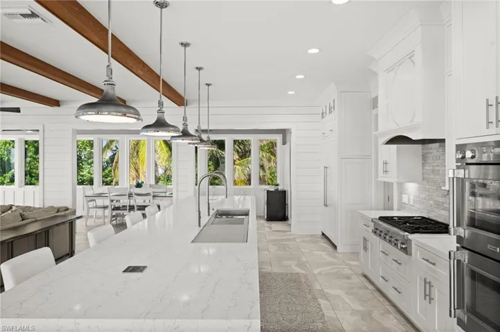 Kitchen with appliances with stainless steel finishes, tasteful backsplash, white cabinetry, a large island, and recessed lighting, five unique hanging light fixtures and double faucets.