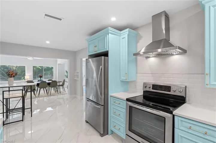 Kitchen with wall chimney range hood, light countertops, blue cabinetry, visible vents, and stainless steel appliances