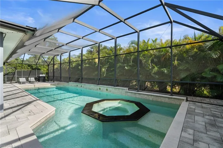 View of swimming pool featuring a patio, a pool with connected hot tub, and glass enclosure