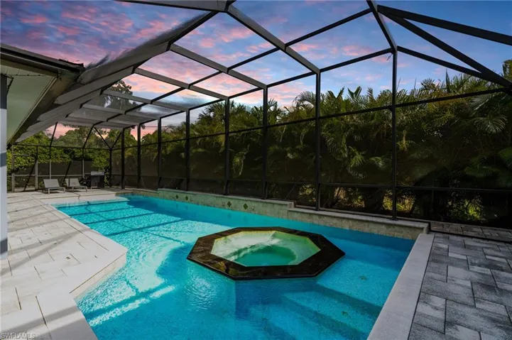 Pool at dusk with a patio area, a pool with connected hot tub, and a lanai