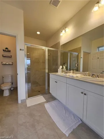Bathroom featuring visible vents, double vanity, toilet, a sink, and a stall shower