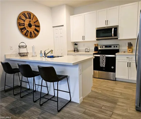 Kitchen featuring a sink, white cabinetry, a breakfast bar area, a peninsula, and stainless steel appliances
