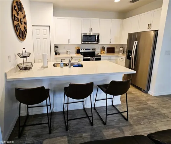 Kitchen featuring a kitchen bar, white cabinetry, a sink, and stainless steel appliances