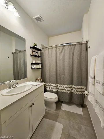 Bathroom featuring vanity, toilet, a textured ceiling, tile patterned floors, and visible vents