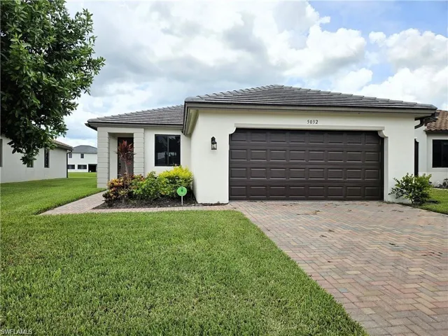 View of front of house featuring stucco siding, a front lawn, a tiled roof, decorative driveway, and a garage