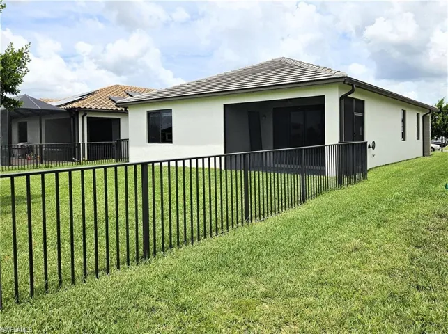 Rear view of house featuring fence, a lawn, stucco siding, and a tiled roof