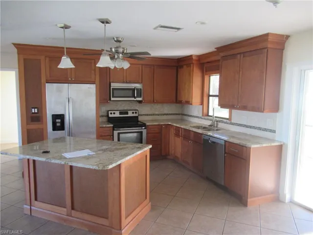 Kitchen with stainless steel appliances, sink, a center island, light tile patterned floors, and light stone counters
