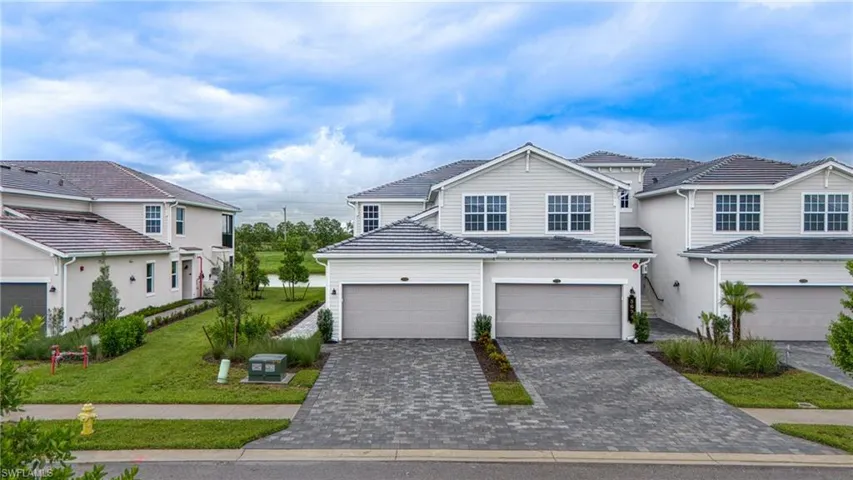 Modern townhome with attached garage, paver driveway, light siding, and landscaping