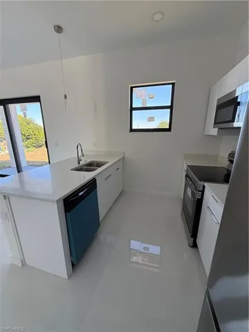 Kitchen with a peninsula, stove, white cabinets, light stone counters, and healthy amount of natural light